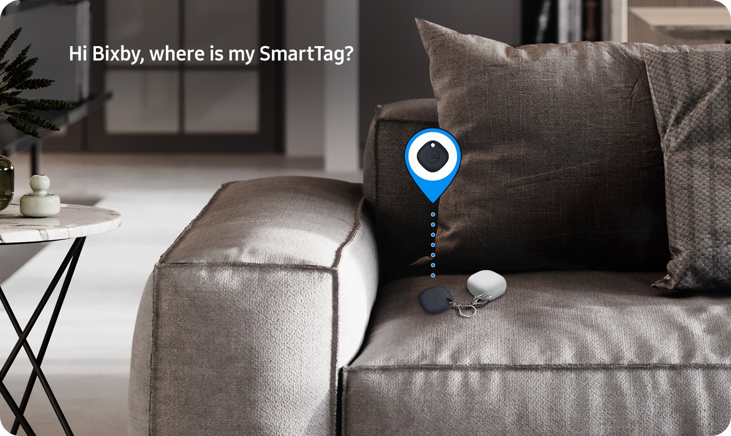 Une Smart Tag repose sur un canapé, connecté à un autre petit appareil Galaxy. Une icône de localisation GPS avec la Smart Tag au centre dépasse de la Smart Tag. Dans le coin supérieur gauche, un texte indique « Bonjour Bixby, où est mon SmartTag? »