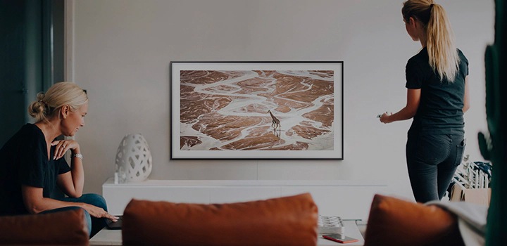 Le téléviseur The Frame repose sur le mur du salon. Une femme est assise à gauche du téléviseur et une autre est debout à droite. Le téléviseur The Frame offre une expérience exceptionnelle, peu importe l’endroit où vous vous trouvez dans la pièce.