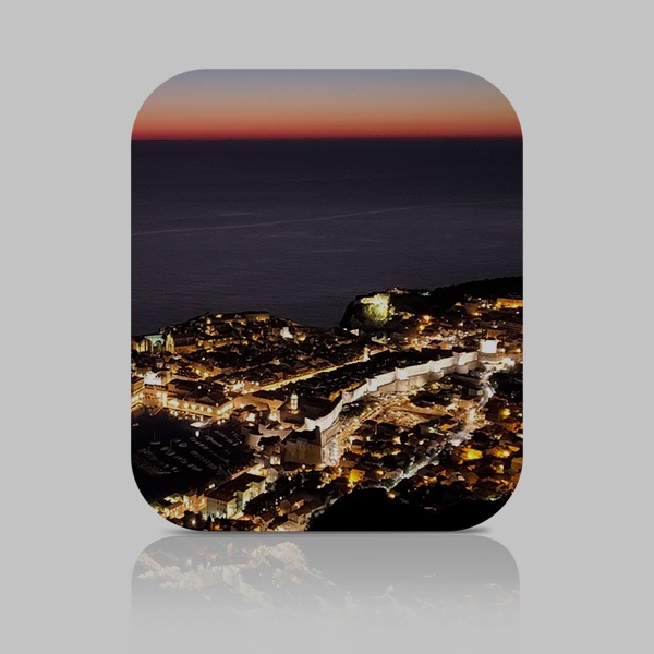 Eine nächtliche Luftaufnahme von Dubrovnik mit dem Adriatischen Meer im Hintergrund. Die Stadt wird durch die Lichter der Gebäude und Autos erhellt.