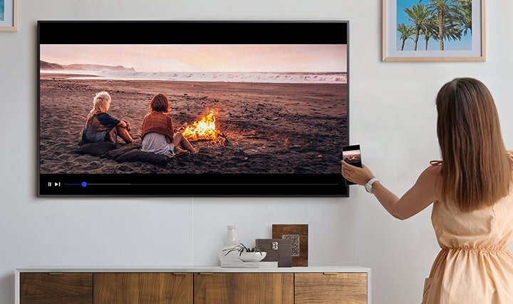 Eine Frau berührt mit ihrem Smartphone den The Frame und spiegelt so ihre Inhalte auf den grossen Bildschirm.