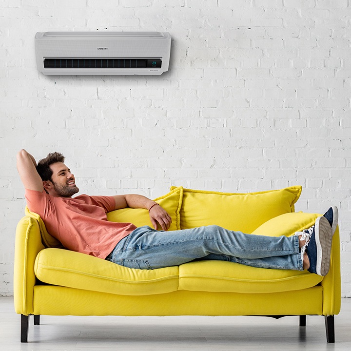 Se ve una persona acostada en un sillón amarillo, disfrutando de la temperatura controlada de un Aire Acondicionado Samsung Documento Aires Acondicionados