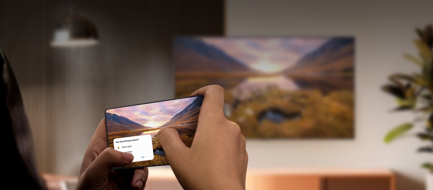 Un teléfono inteligente Galaxy que proyecta la imagen de un paisaje majestuoso en un televisor Samsung que está en el fondo. El televisor muestra exactamente la misma imagen.