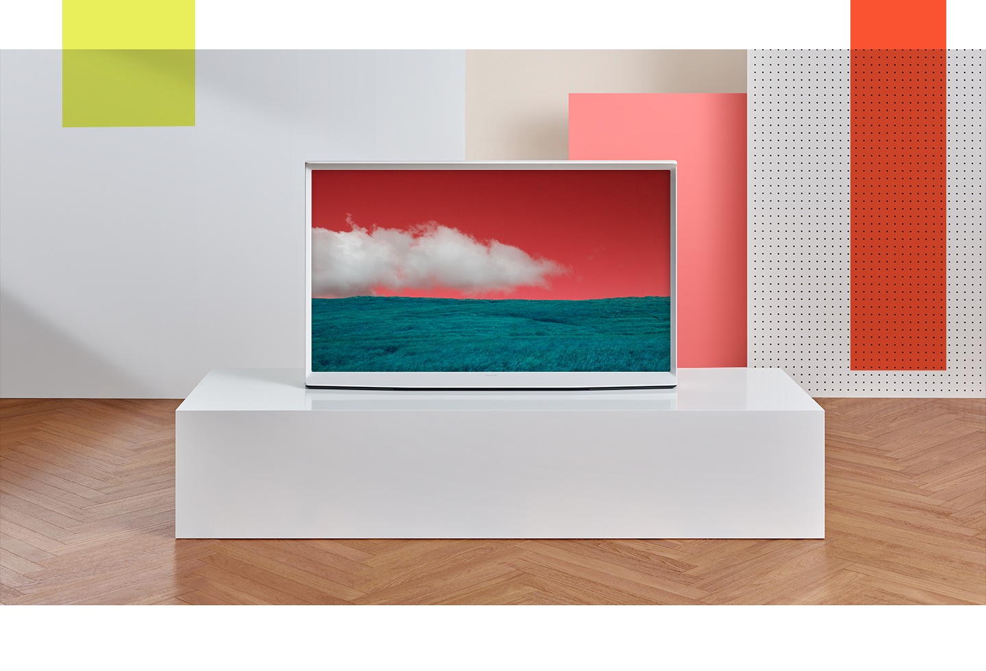 El The Serif Blanco visto desde el frente en un soporte de exhibición de bloque blanco con un vívido verde azulado y un cielo rosado brillante en la pantalla.
