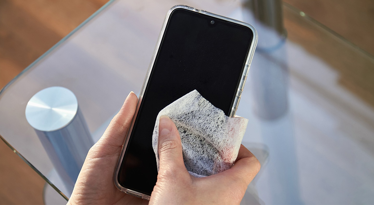 Las manos de una mujer limpian la pantalla de un teléfono inteligente con un paño desinfectante. Mujer en primer plano limpia su teléfono móvil en la calle de una ciudad.