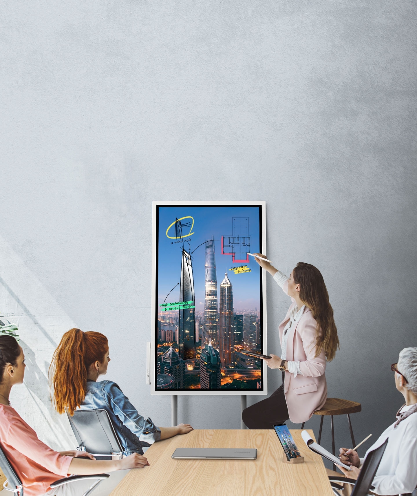 Una imagen que muestra cuatro personas en una reunión donde el dispositivo de Samsung Flip y un smartphone están conectados, mostrando las mismas imágenes. Están mirando la pantalla del Samsung Flip en modo vertical y dos de ellos están tomando notas.
