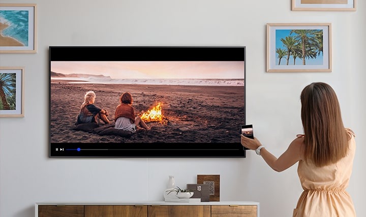 The Frame TV ukazuje zrcadlení obsahu displeje smartphonu, který drží žena, jednoduchým klepnutím na TV v telefonu.