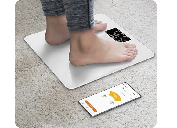 Ein Galaxy-Nutzer steht auf einer Waage, die mit der Samsung-Health-App auf einem Galaxy-Gerät verbunden ist, die das Gewicht des Nutzers anzeigt.