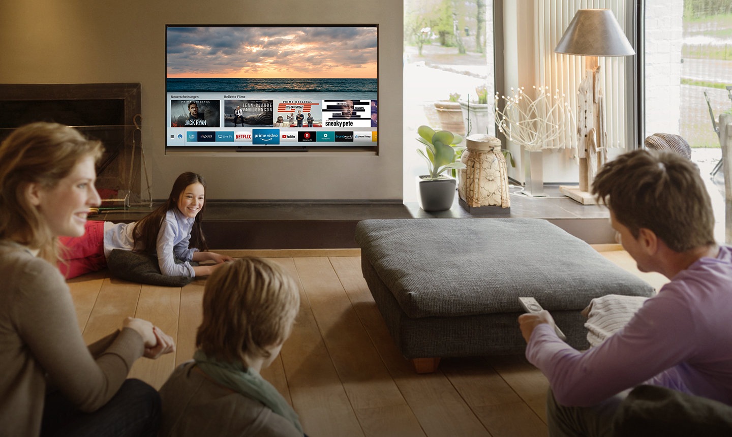 Smart ist jetzt auch intelligent Eine gruppe von Personen schaut Smart TV im Wohnzimmer und die Smart HUB Benutzeroberfläche wird auf einem TV Bildschirm gezeigt. Die Oberfläche enthält verschiedene Inhalte, wie z.B. "Was ist neu", "Schauen Sie danach" und verschiedene Anwendungen wie Netflix, Amazon Prime Video, Youtube, Facebook Video, Google Play Movies & TV, SmartThings, Galerie, Internet.