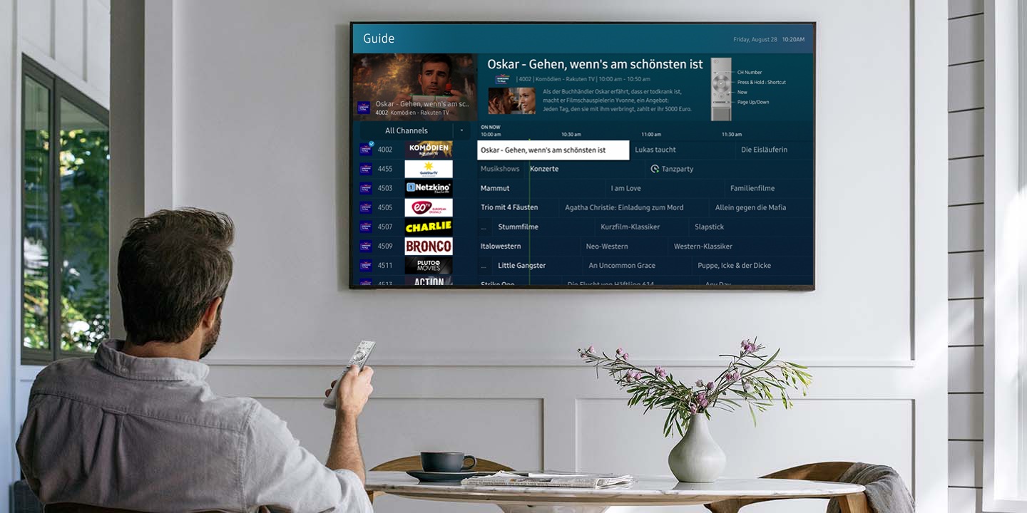 Samsung Smart TV verfügt über Samsung TV Plus-Kanäle. Ein sitzender Mann sucht nach Fernsehkanälen mit einer Fernbedienung. Es wird der Programmguide von Samsung TV Plus gezeigt.