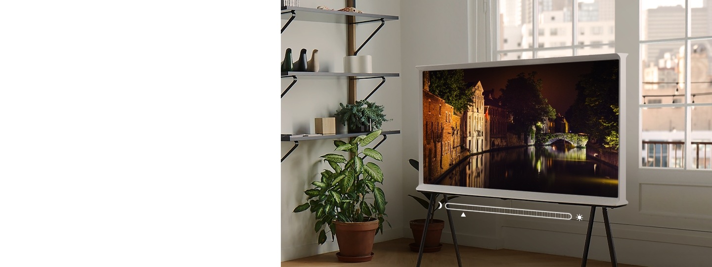 Video zu Adaptive Picture Ein The Serif in Cloud White steht auf einem TV-Möbel in einem Wohnzimmer und zeigt eine nächtliche Szene aus einer alten Stadt, wobei sich die Steingebäude mit Hilfe von Adaptive Picture wunderschön auf dem Wasser spiegeln.