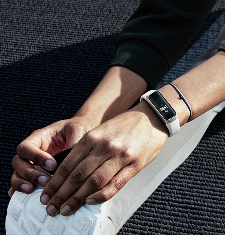 En kvinde strækker ud og bøjer sig fremad for at tage fat i sine sko med et Galaxy Fit om håndleddet