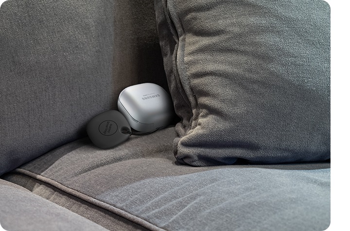 En un sofá aparecen unos Galaxy Buds unidos a un SmartTag medio tapados por un cojín.