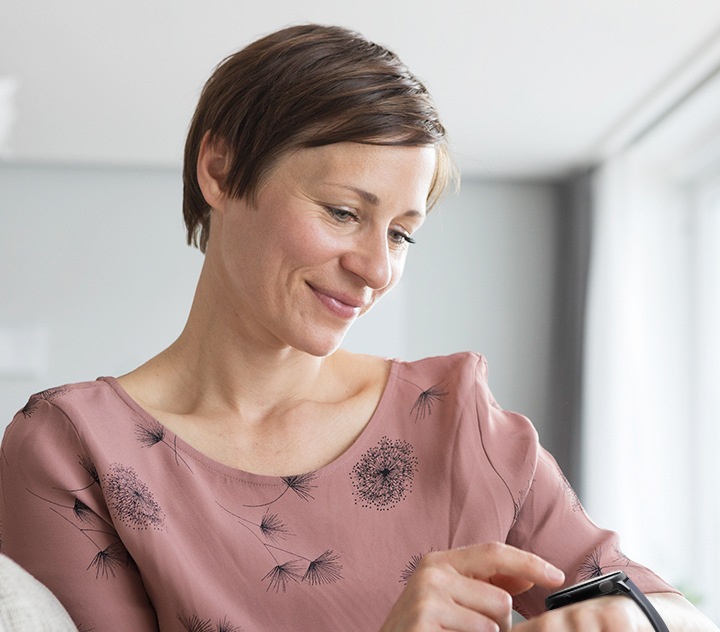 Una mujer de mediana edad, que sonríe y mira a su Galaxy Watch, está a punto de hacer un gesto con el dedo.