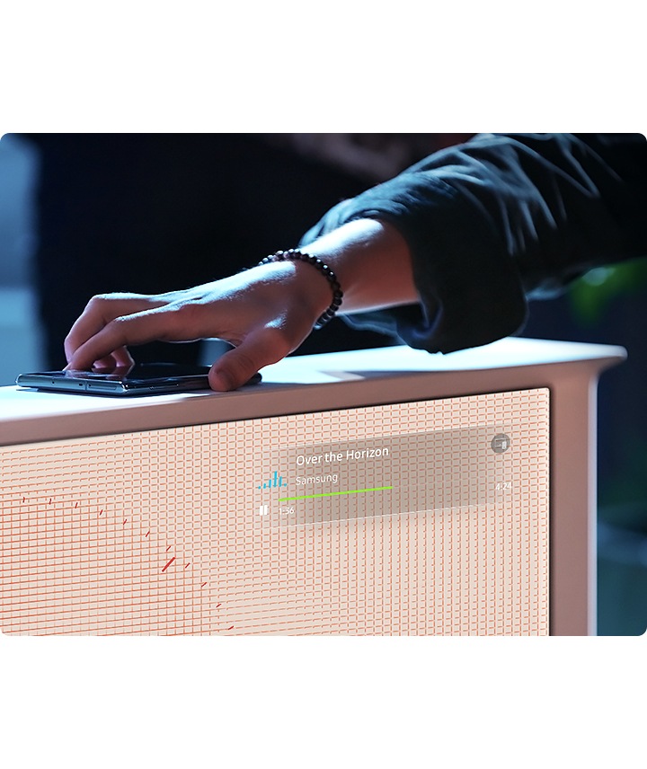Mientras alguien pone un smartphone con NFC encima del televisor, The Serif muestra que la canción “Over the Horizon” está sonando en este momento. Está enseñando cómo conectar el teléfono al televisor con The Serif NFC de Samsung.