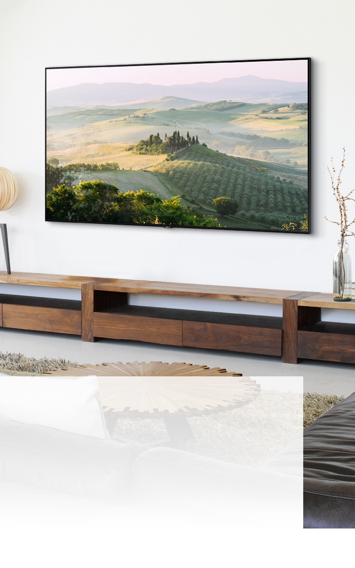 Un televisor de pantalla grande montado en la pared que muestra un paisaje rural en una sala de estar iluminada por el sol.