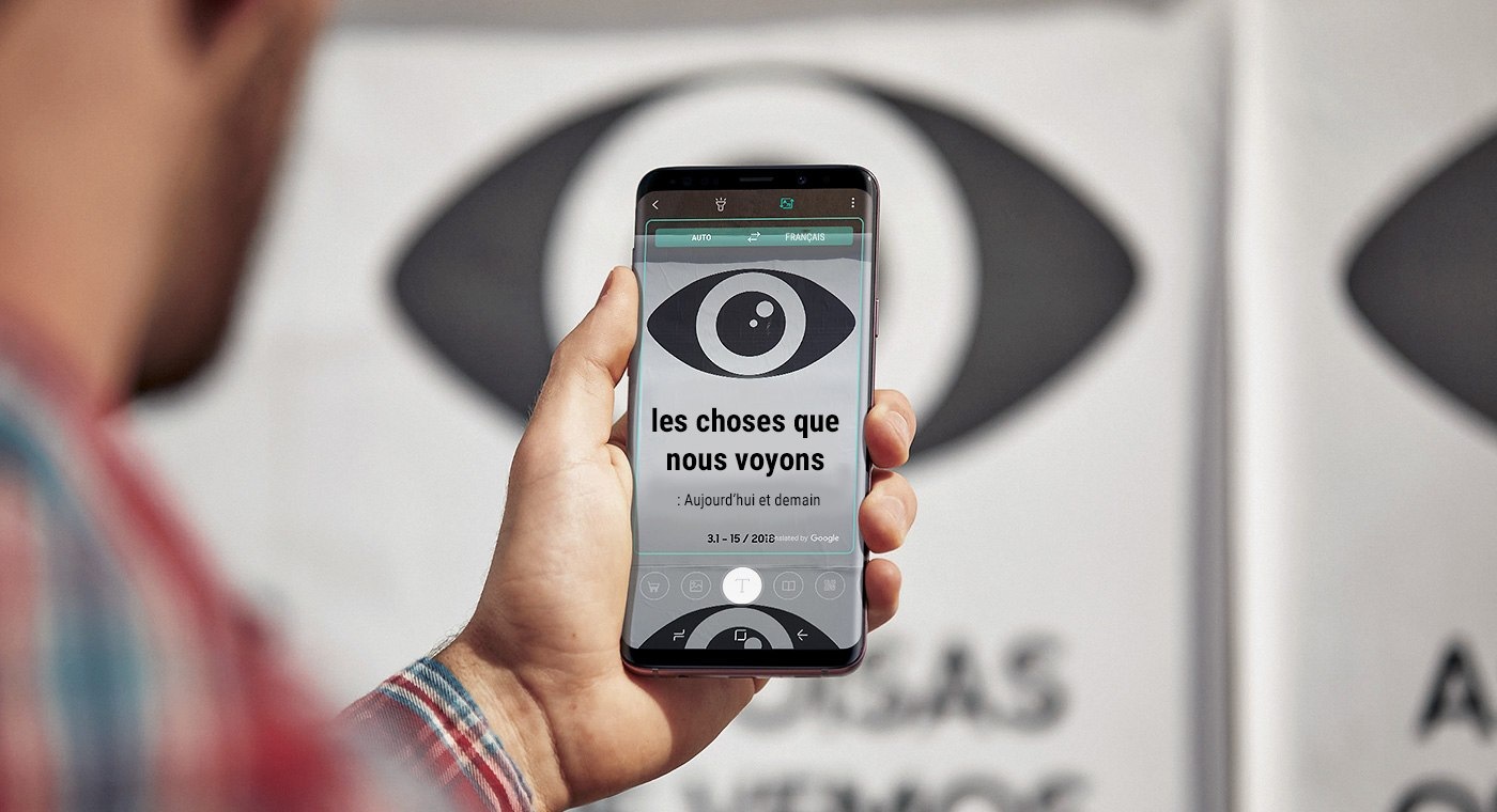 Une photo d'une personne tenant un Galaxy S9+ montrant un panneau traduit, avec l'image non-traduite en arrière-plan