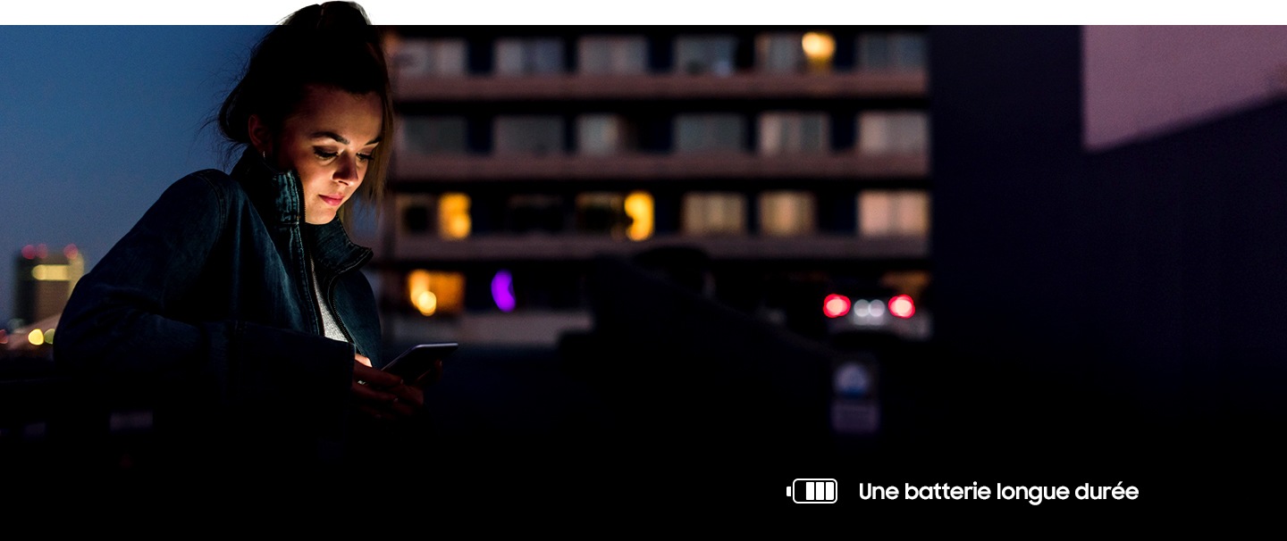 Photo d'une femme utilisant son téléphone durant la nuit. Une icône batterie en bas à droite lui indique qu'il lui reste encore de la batterie.