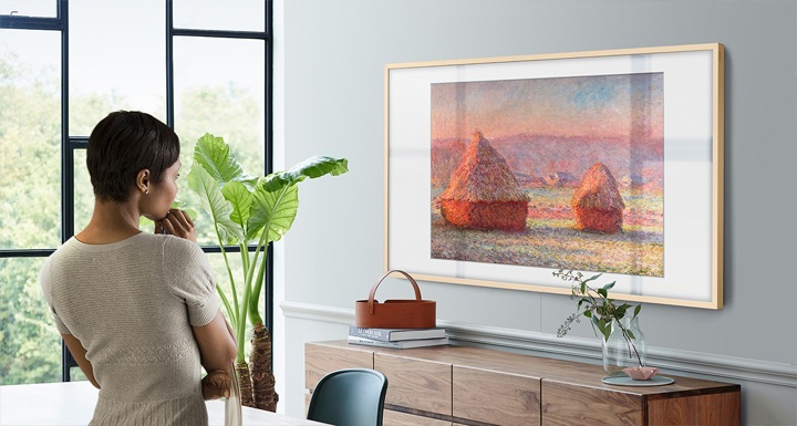 Há um Quadro pendurado na parede da sala de estar mostrando “Celeiros pela manhã, efeito de neve” por Claude Monet. E uma mulher observa e aprecia as pinturas de Monet, arte impressionista que regista a beleza da luz ao pôr do sol.
