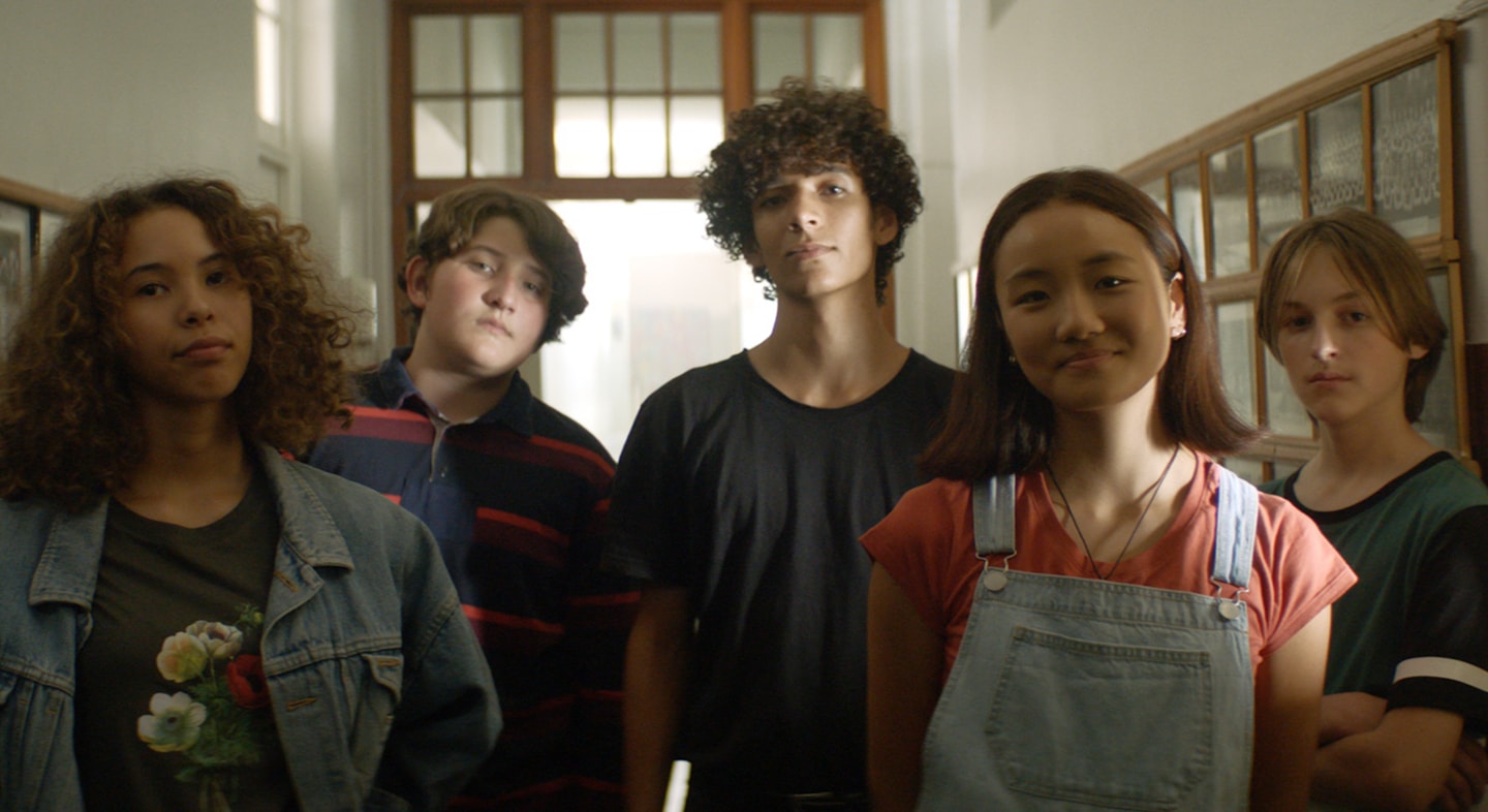 Several kids are standing in a group all staring at the front.