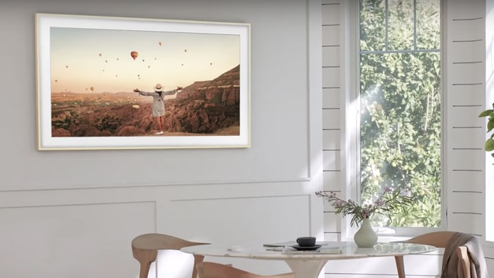 The Frame TV hang på veggen i stuen, og skjermen viser et bilde av en kvinne på toppen av en ås som ser på luftballonger på himmelen.
