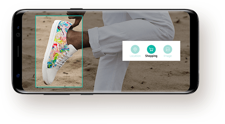Photo of a person who is wearing sneakers holding up one foot on the screen of Galaxy S8 with messages from user to Bixby asking to search for similar sneakers online