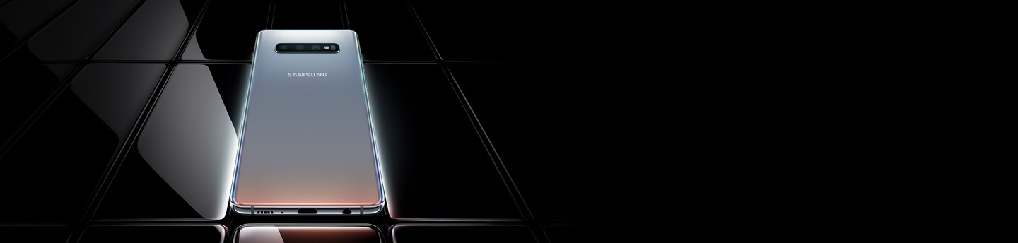 Several Galaxy S10 plus phones all laid flat and seen at an angle from the bottom. All are black except the one in the middle, which is shown with a prismatic white gradient onscreen with Galaxy S10 plus overlaid on top of it and the two phones on either side.