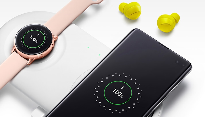 A rose gold Galaxy Watch Active and Galaxy S10 charge on a wireless charging pad, with a pair of yellow Galaxy Buds shown nearby.