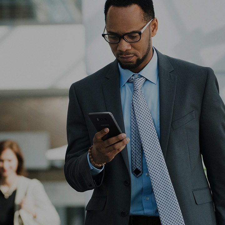 A fully dressed business man looking at his smartphone as he walks out of the building