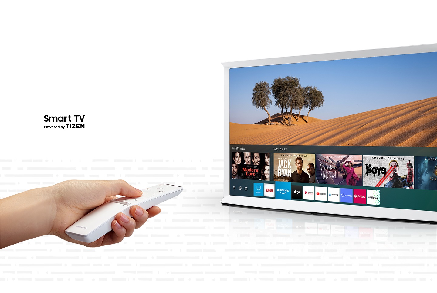 Zaslon modela Serif televizora u nebeski bijeloj boji prikazuje scenu iz pustinje, a pri dnu zaslona vidimo Smart Hub sučelje. Lijevo vidimo ruku kako drži bijeli Samsung One daljinski upravljač usmjeren prema televizoru. Serif televizor pametni je televizor pokretan operativnim sustavom Tizen.