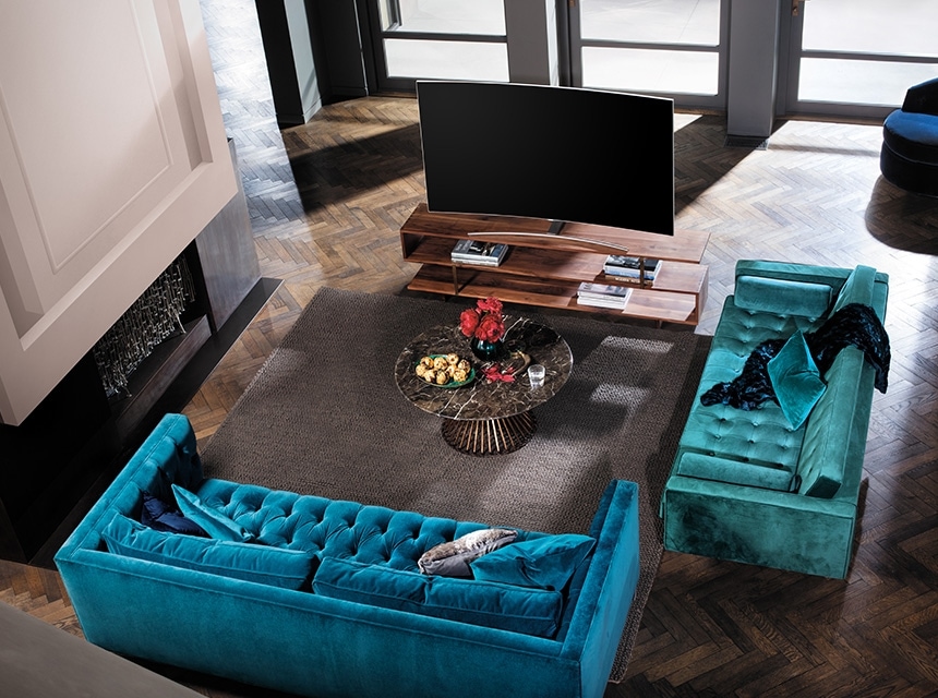 A nappali enyhén távoli nézetből, ahol a QLED TV egy keményfa asztalon helyezkedik el, előtte egy kis asztal és kanapé látható.
