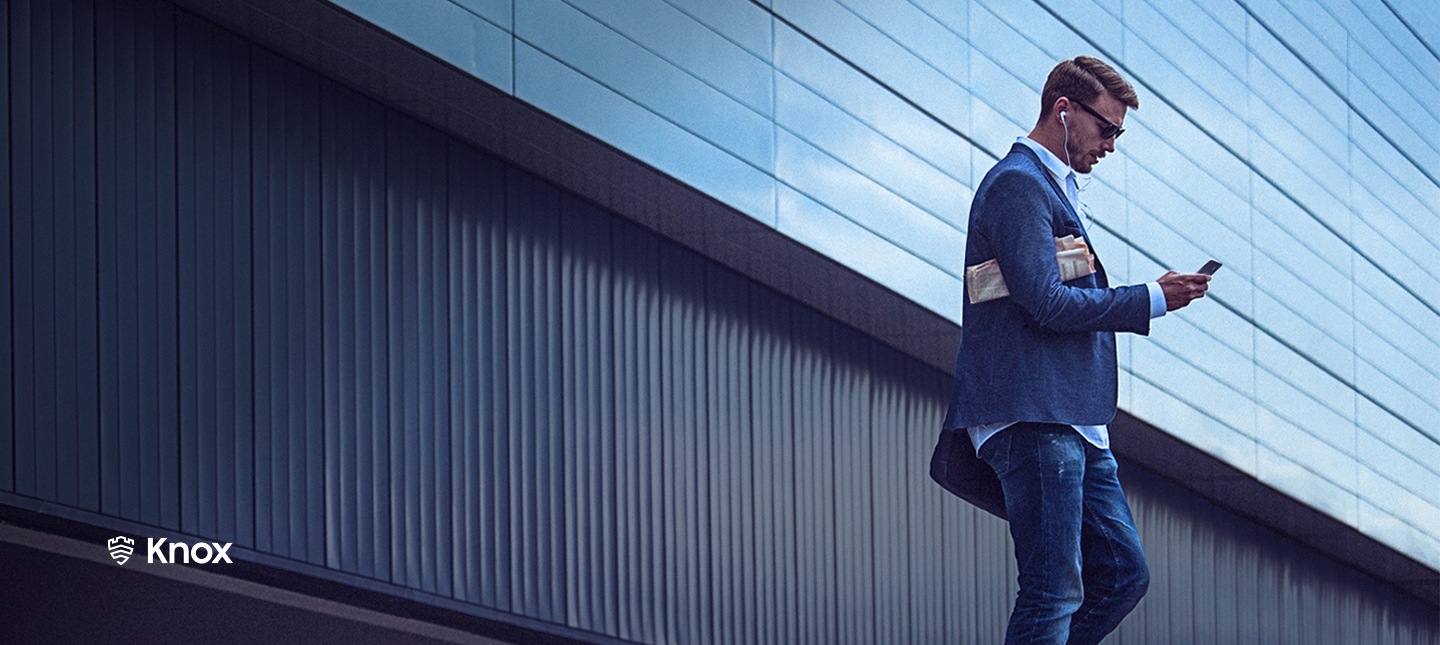 A man is looking at his smartphone that protected by Samsung Knox