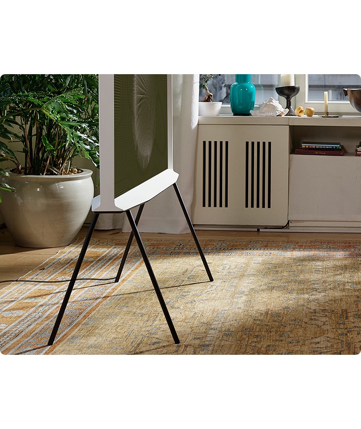 The bottom half of a Cloud White model of The Serif is shown from the side on a black stand in a neat living room.