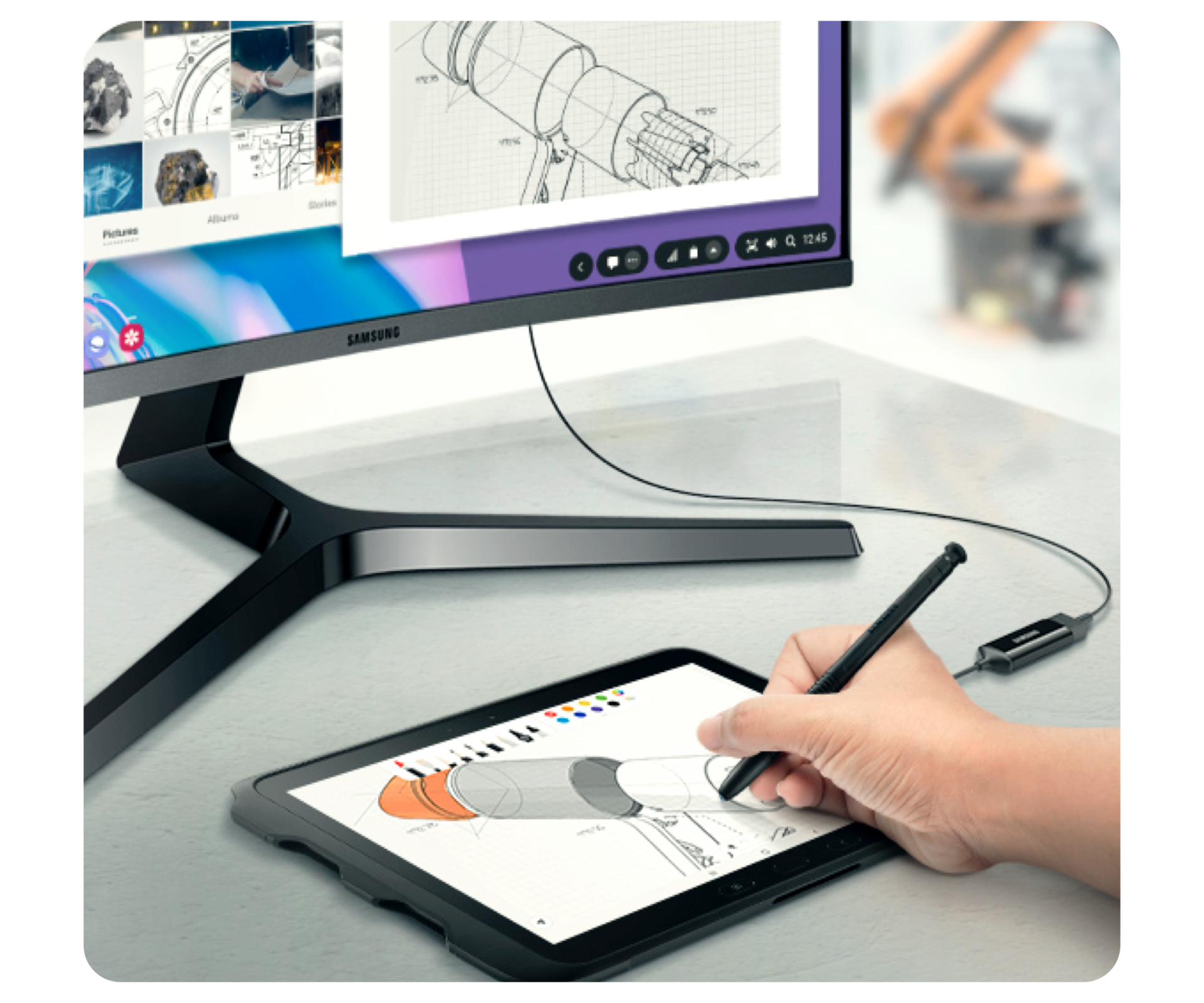 A Samsung curved monitor on a grey desk connected to a Samsung tablet. A hand is using a black S Pen to draw on the tablet.