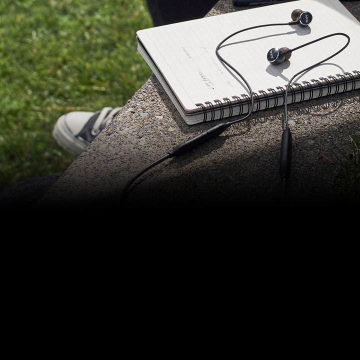 In-ear Headphones AKG Y100 wireless earphones on top of a note pad