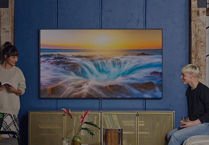 Two women either size of a Samsung TV mounted to the wall