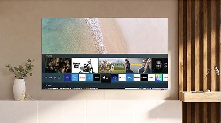 טלוויזיה חכמה של Samsung תלויה על קיר ומציגה את אפליקציית Apple TV, עם גישה לתכנים של Apple TV +.