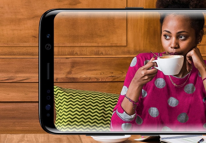 A woman taking a sip of her coffee in a café seen through a Samsung Galaxy S8 screen
