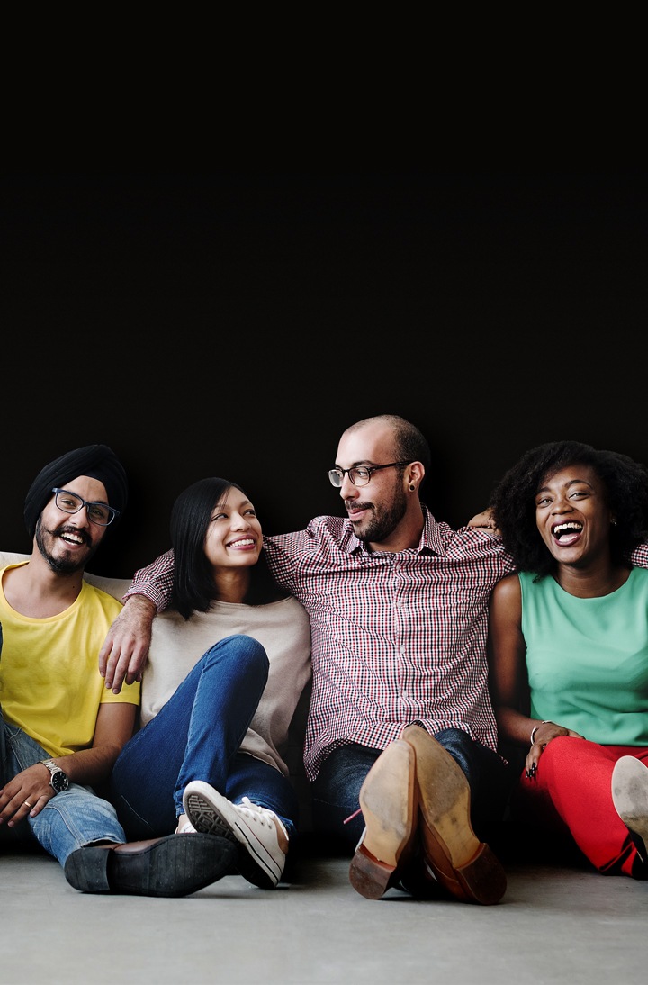 Four people are sitting together by putting arms around each other's shoulders.