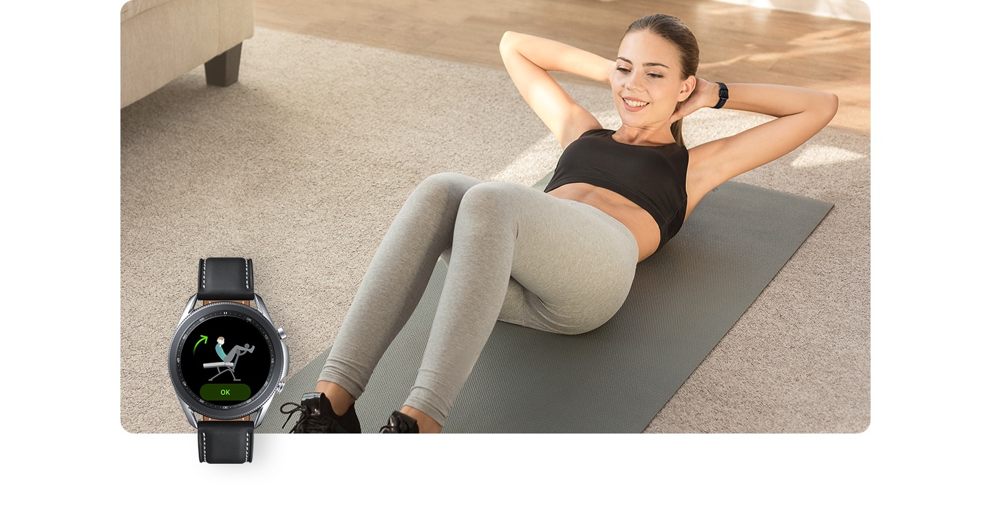 Una donna che indossa un Galaxy Watch fa esercizi per gli addominali su un tappetino dentro casa. In primo piano, il display di un Galaxy Watch monitora i suoi movimenti.