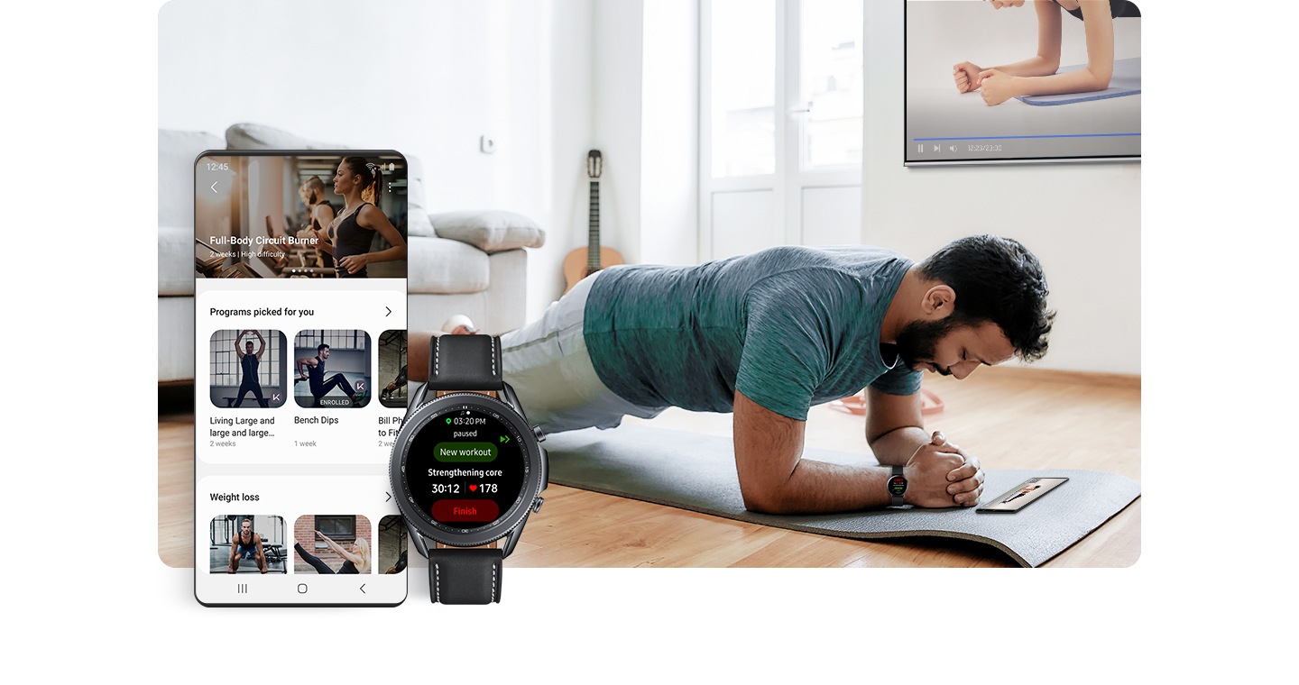 Un uomo che indossa un Galaxy Watch mantiene una posizione di plank su un tappetino dentro casa. Il suo programma di allenamento è visibile su uno smartphone appoggiato a terra e sul TV appeso a una parete. In primo piano, una schermata di interfaccia grafica mostra vari programmi di allenamento. Il display di un Galaxy Watch mostra il nome dell’allenamento e il battito cardiaco.