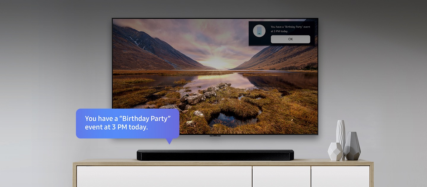 Televisore Samsung al centro e una soundbar posizionata in basso. Una vignetta con testo blu dalla soundbar recita: “Oggi hai una festa di compleanno alle ore 15.00”. Nell’angolo in altro a destra della TV appare un avviso con lo stesso promemoria e sotto il pulsante “OK”.