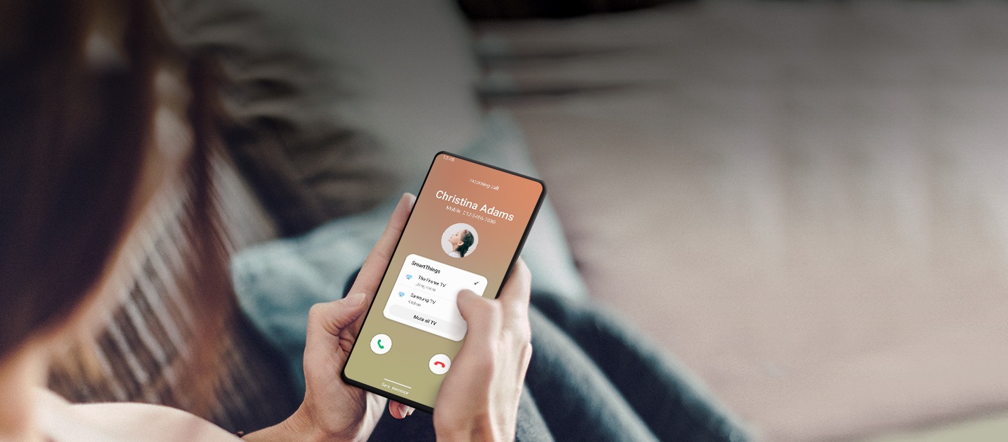 Una persona seduta sul divano guarda il suo smartphone Galaxy mentre sta entrando una chiamata di Christina Adams.