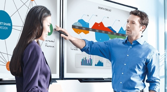 Un uomo che indica lo schermo di un display mentre discute con un collega nella sala conferenze