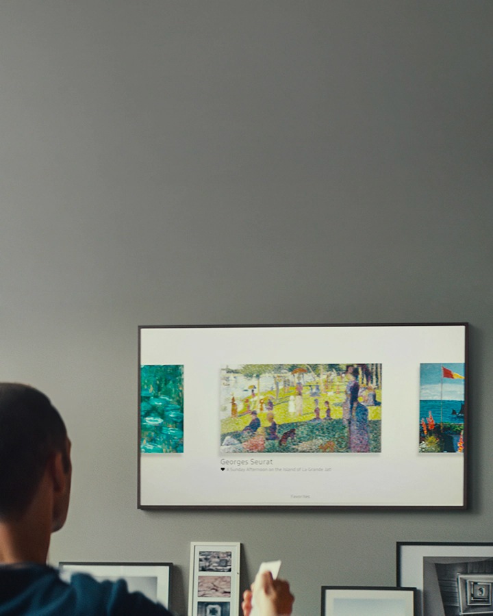 Un ragazzo, seduto davanti al The Frame tiene in mano un telecomando e sceglie tra i vari dipinti mostrati sul TV quello da impostare su suo televisore Samsung.