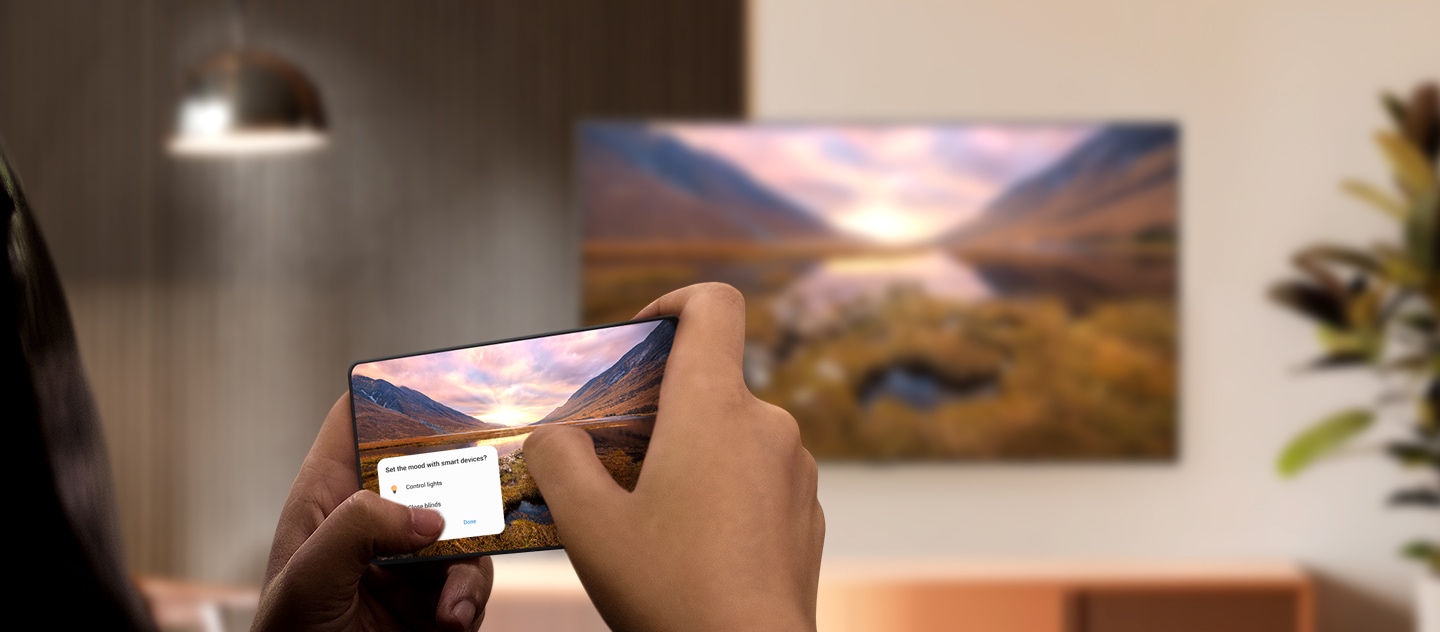 A Galaxy smartphone casting a majestic landscape image onto a Samsung TV in the background. The TV displays the identical landscape image.