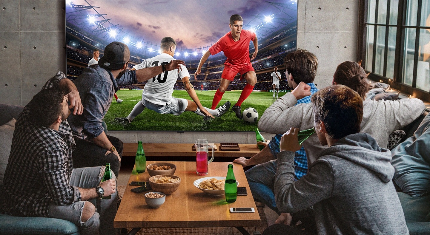 5 men sitting around a mini table with snacks and beverages are watching football game on the large screen TV. With Samsung Super Big TV, size of living space is no longer a factor.