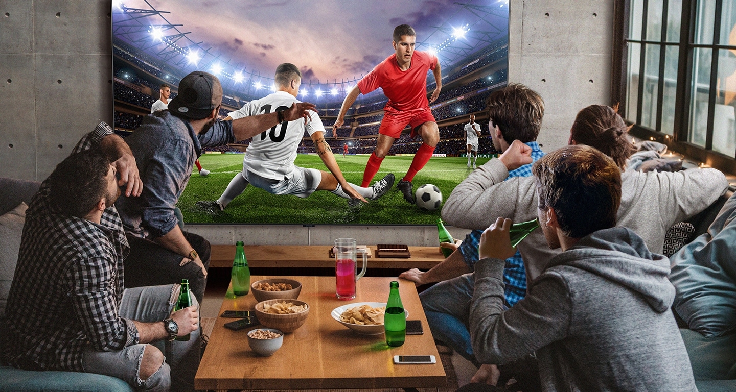 5 men sitting around a mini table with snacks and beverages are watching football game on the large screen TV. With Samsung Super Big TV, size of living space is no longer a factor.