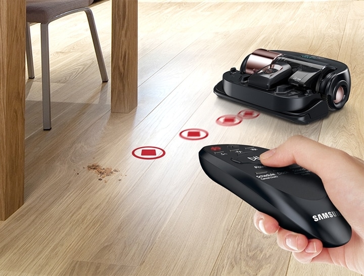 A remote control point to the dust and a robot vacuum is approaching to the dust.