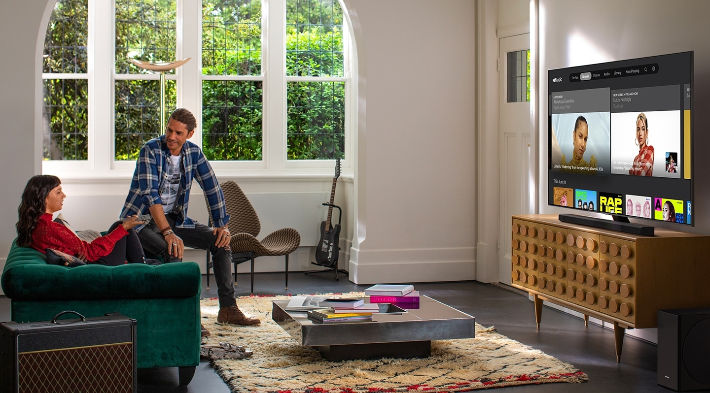 A man and woman sit in the living room and browse through the Apple Music app on a Samsung Smart TV.