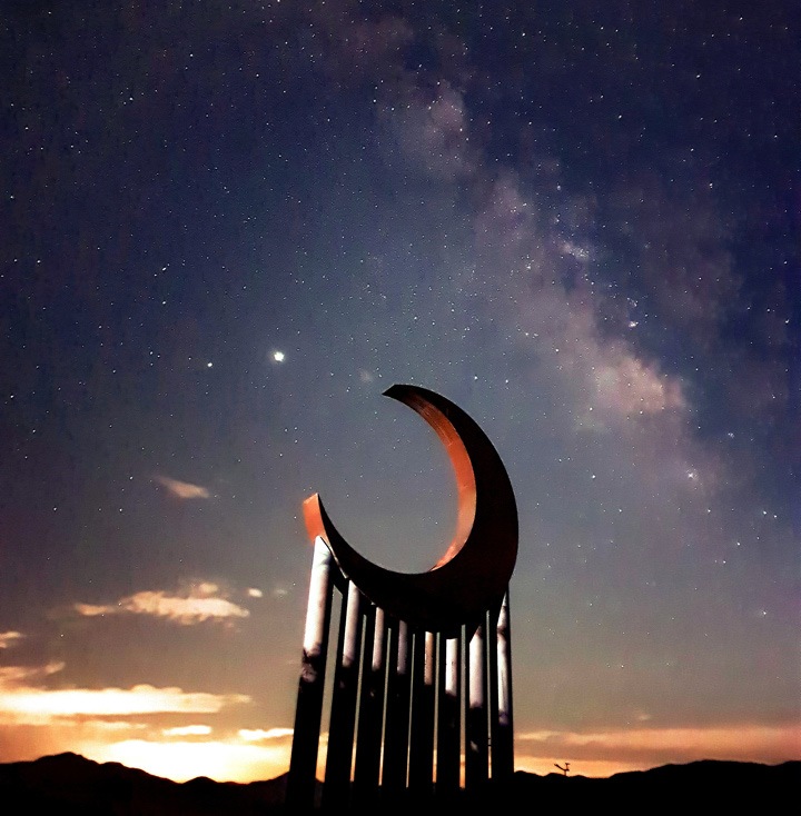 Sculpture of a moon, supported by columns against a starry night sky during sunset
